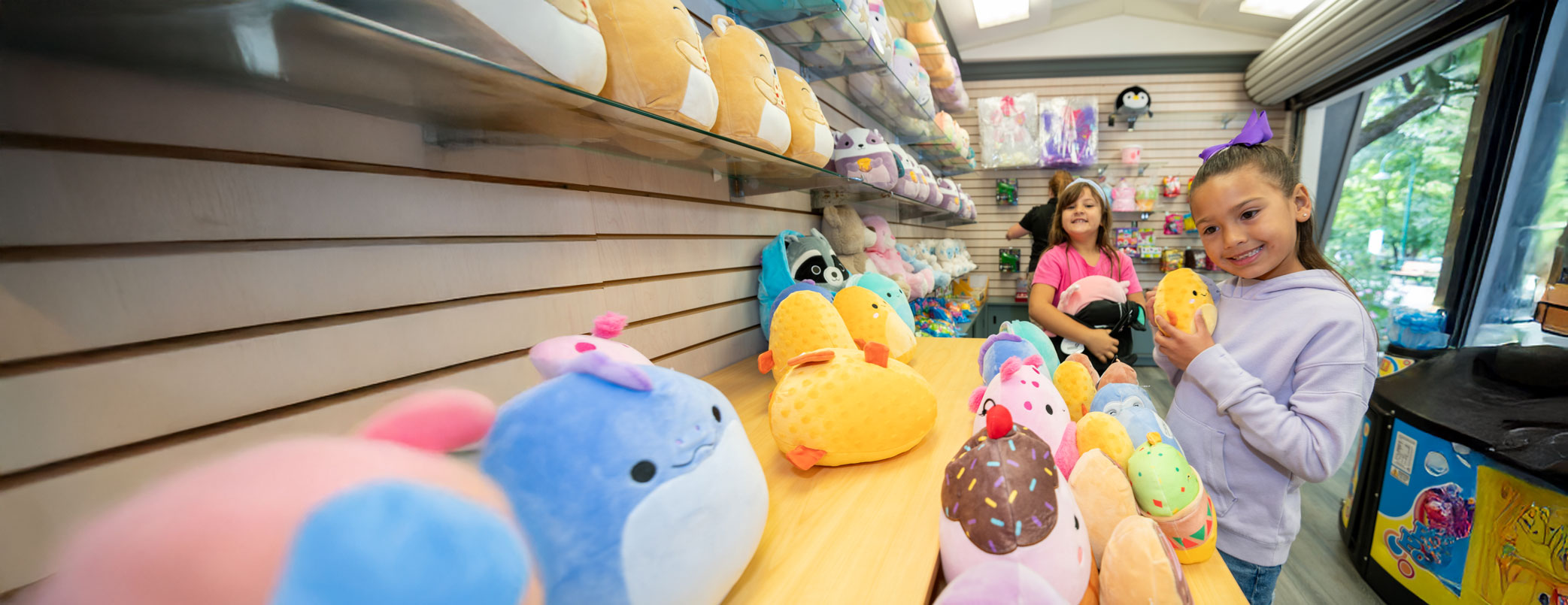 Young girl in purple sweater and bow holding a yellow stuffed animal and girl in pink shirt holding a black and pink stuffed animal