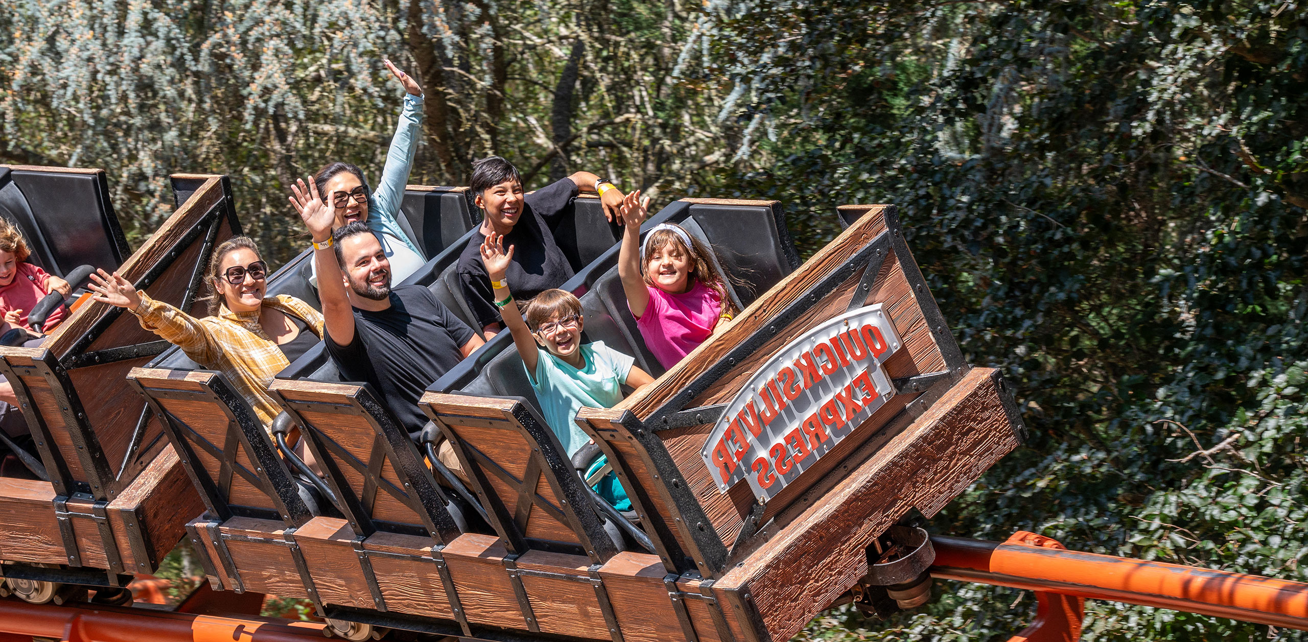 Guests on the Quicksilver Roller Coaster with their hands in the air and smiling