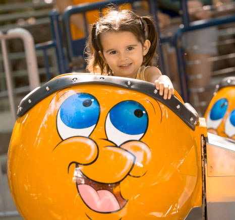 Little girl in yellow tank tip and pony tails smiling while on Bulgy the Goldfish ride