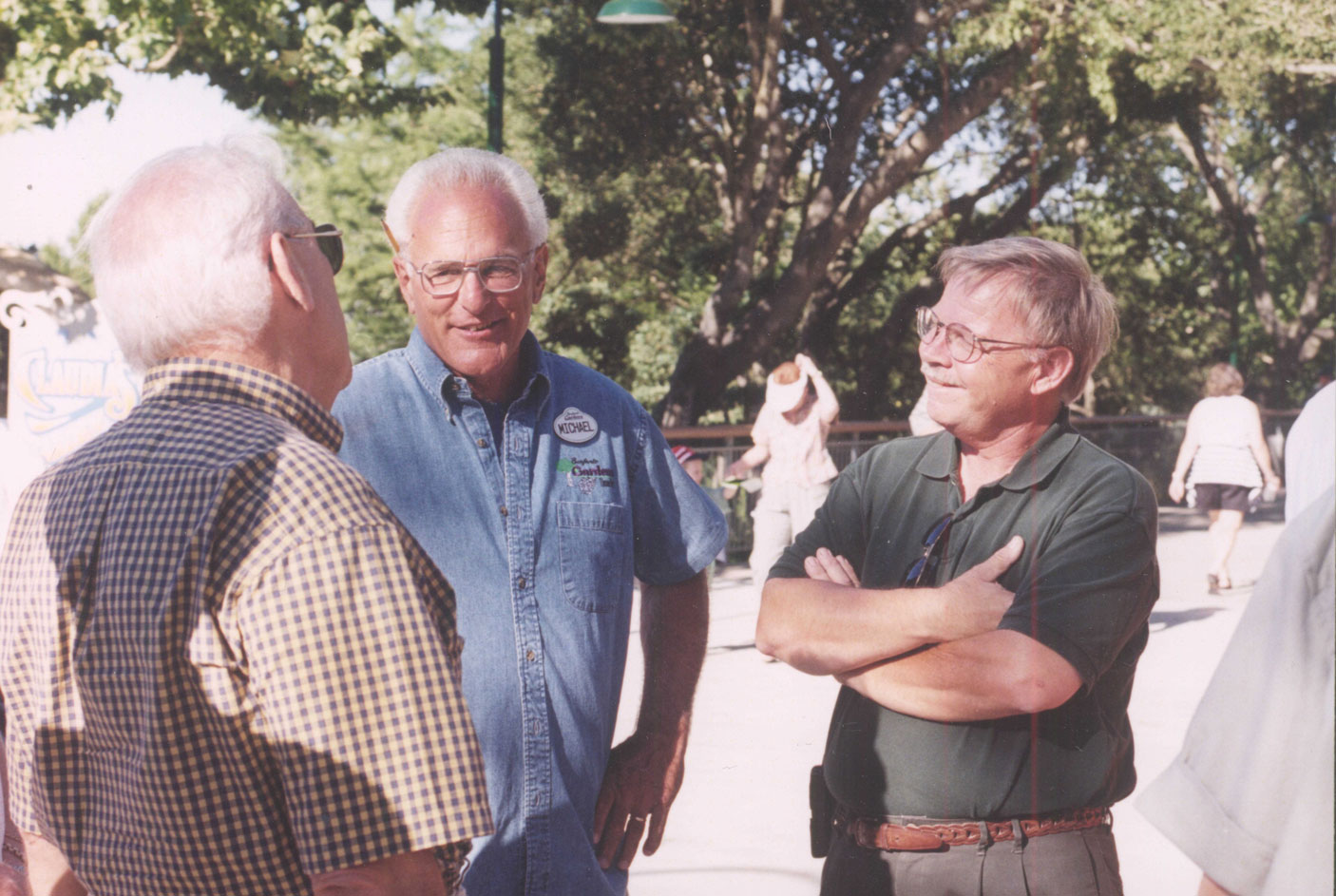 Three men smiling and talking to each other with large green trees behind them