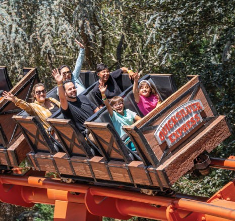 Guests on the Quicksilver Roller Coaster with their hands in the air and smiling