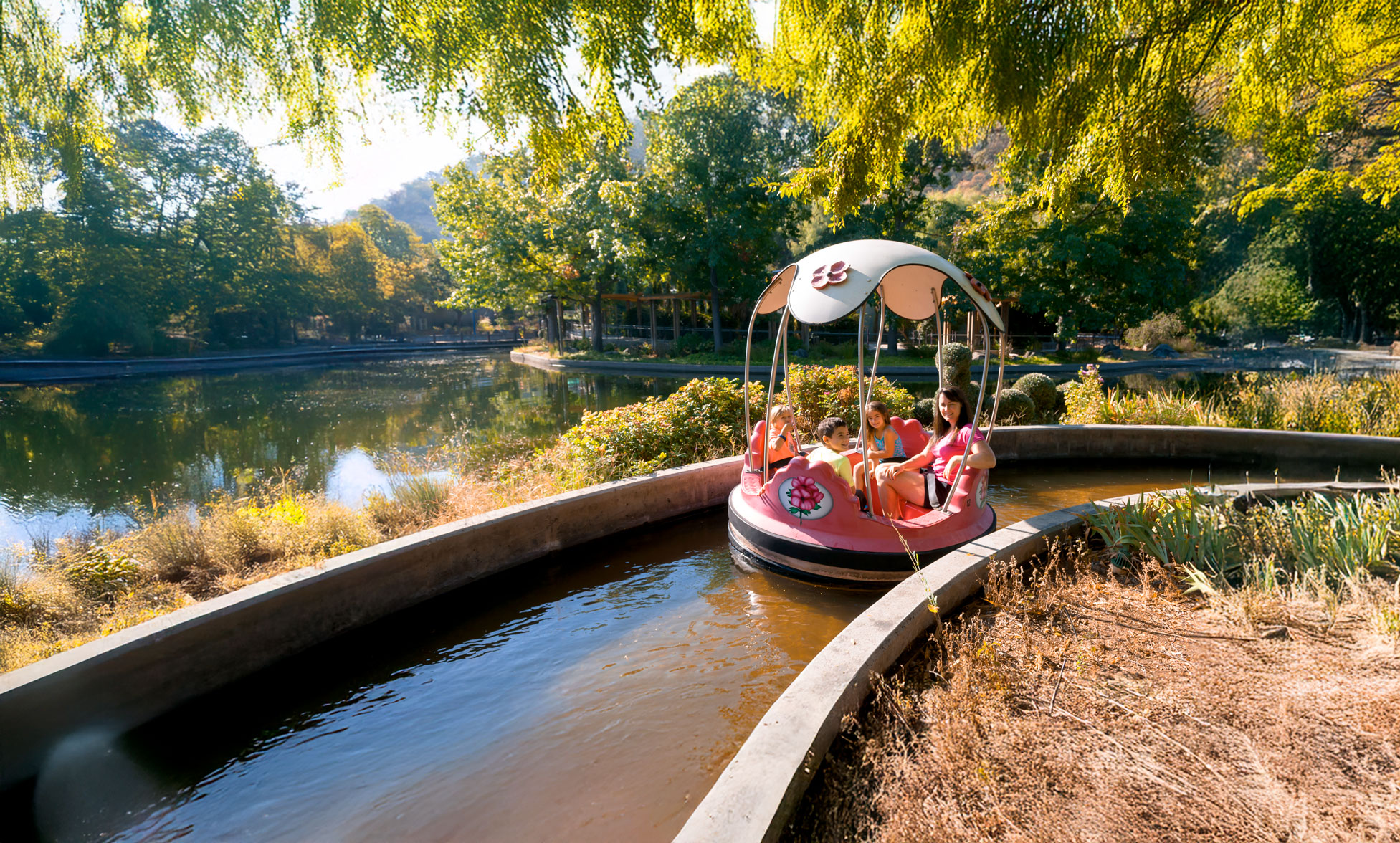 Mother in pink shirt with her three children riding the Rainbow Garden Round Boats ride on a sunny day