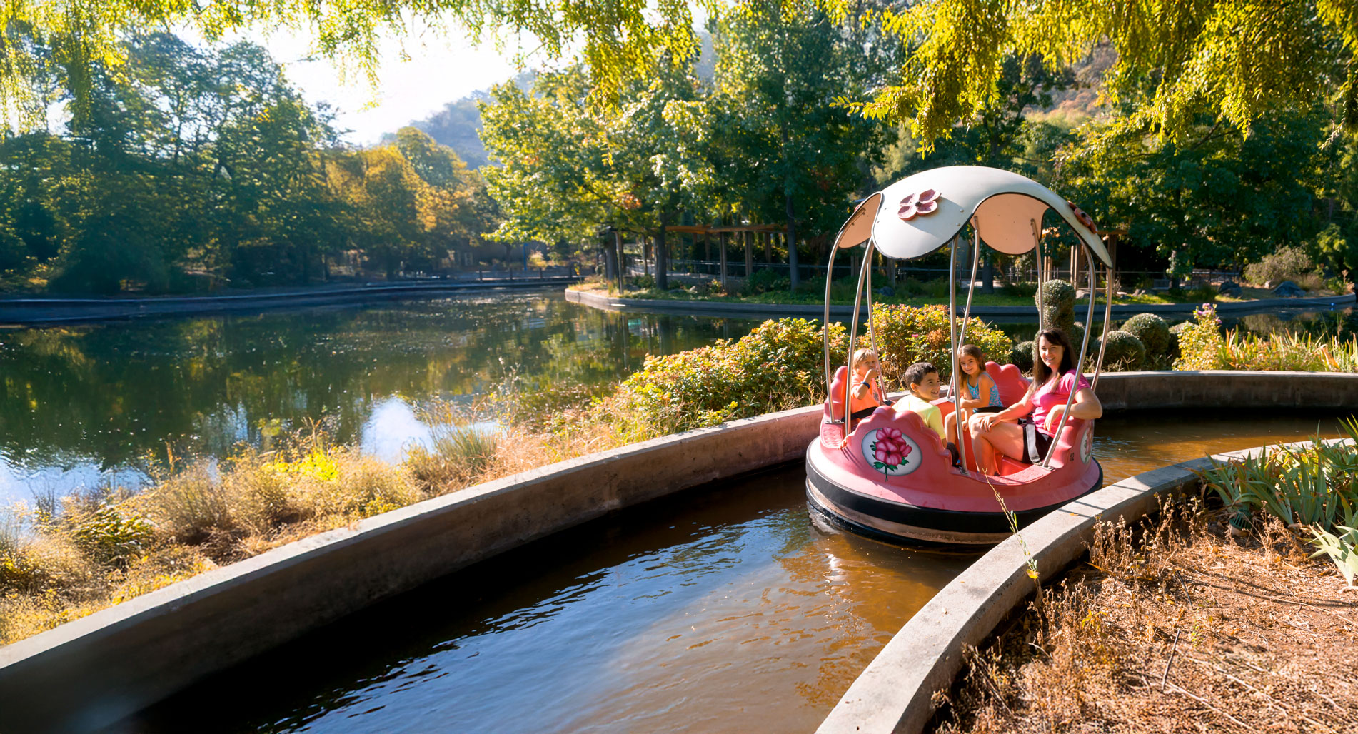 Mother in pink shirt with her three children riding the Rainbow Garden Round Boats ride on a sunny day