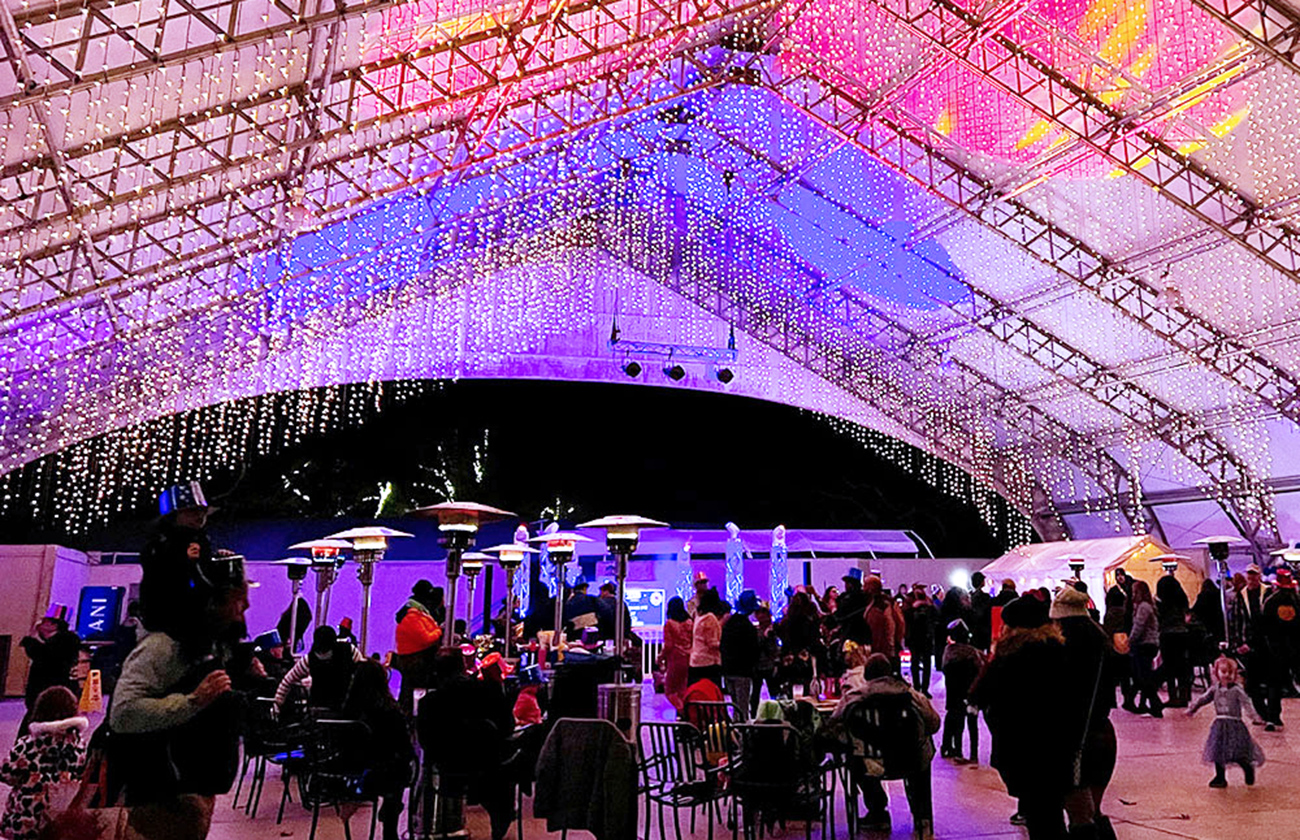 Dangling white lights hanging from the ceiling and people dancing at Events Plaza at night