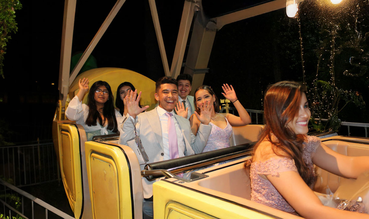 Teens in prom attire smiling with their hands up on the Banana Split ride