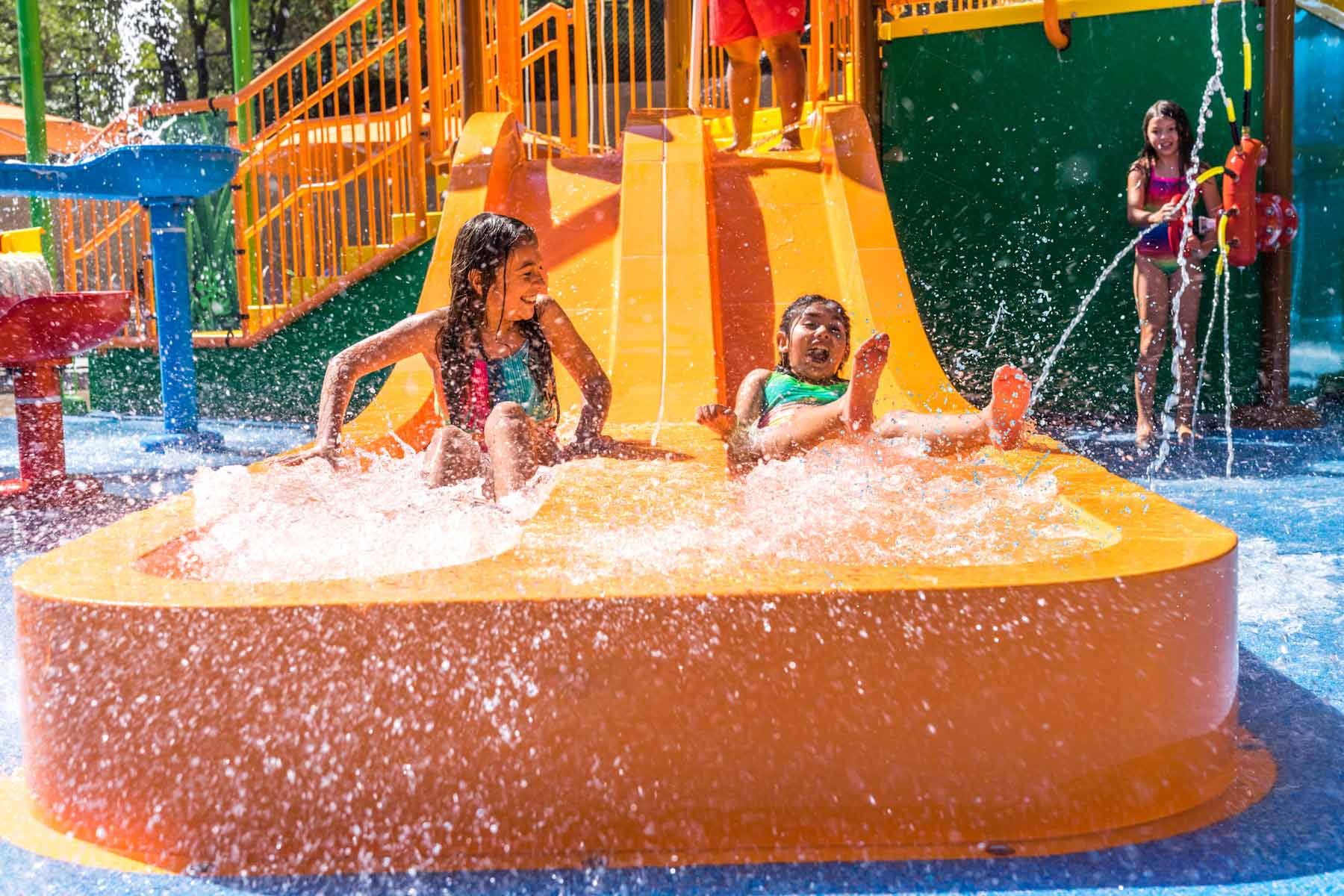 Two young girls in colorful swimsuits going down an orange water slide at Water Oasis