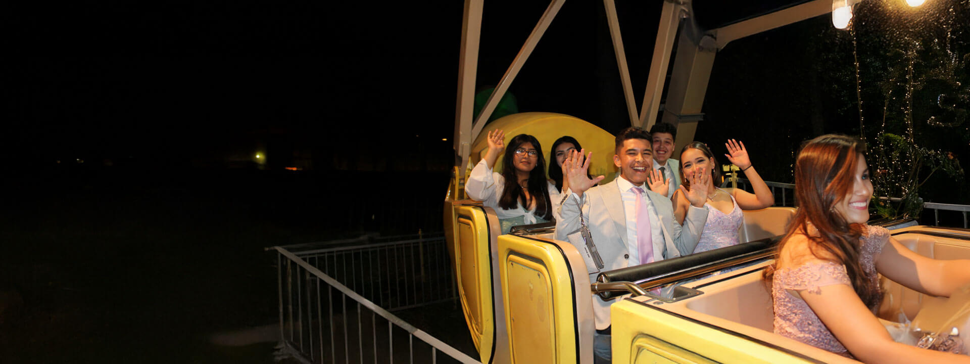 Teens in prom attire smiling with their hands up on the Banana Split ride