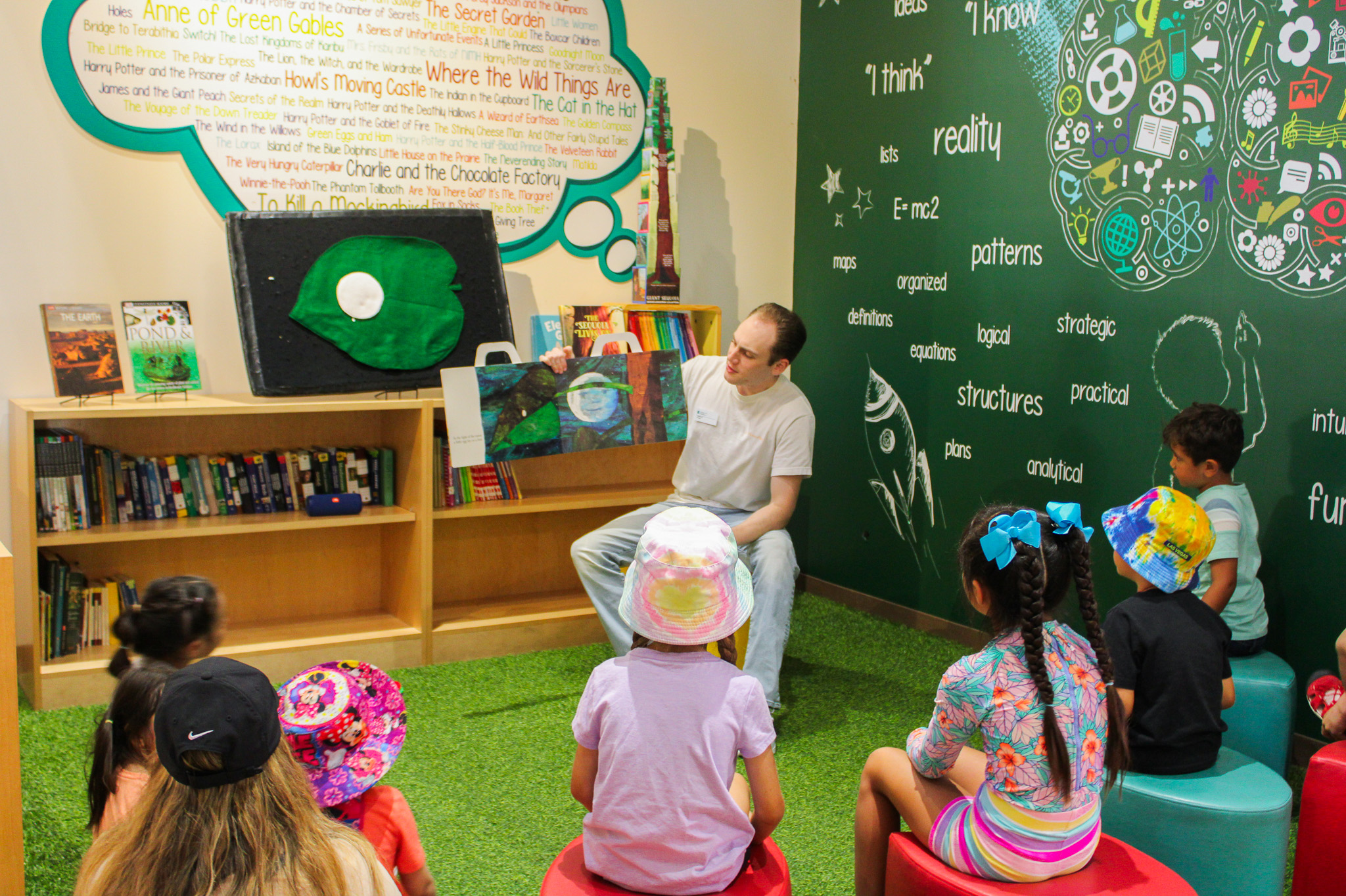 Man holding up a book while reading it to children sitting around him.