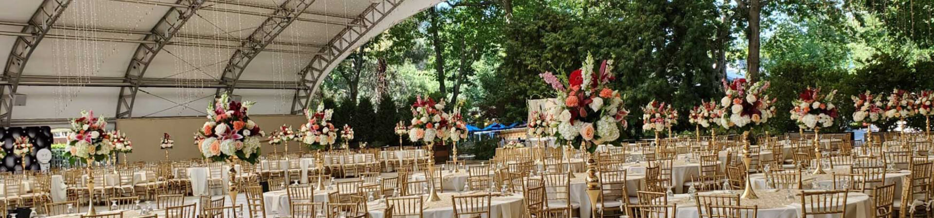 Light brown chairs around circular tables with white table covers and flower arraignments on top.
