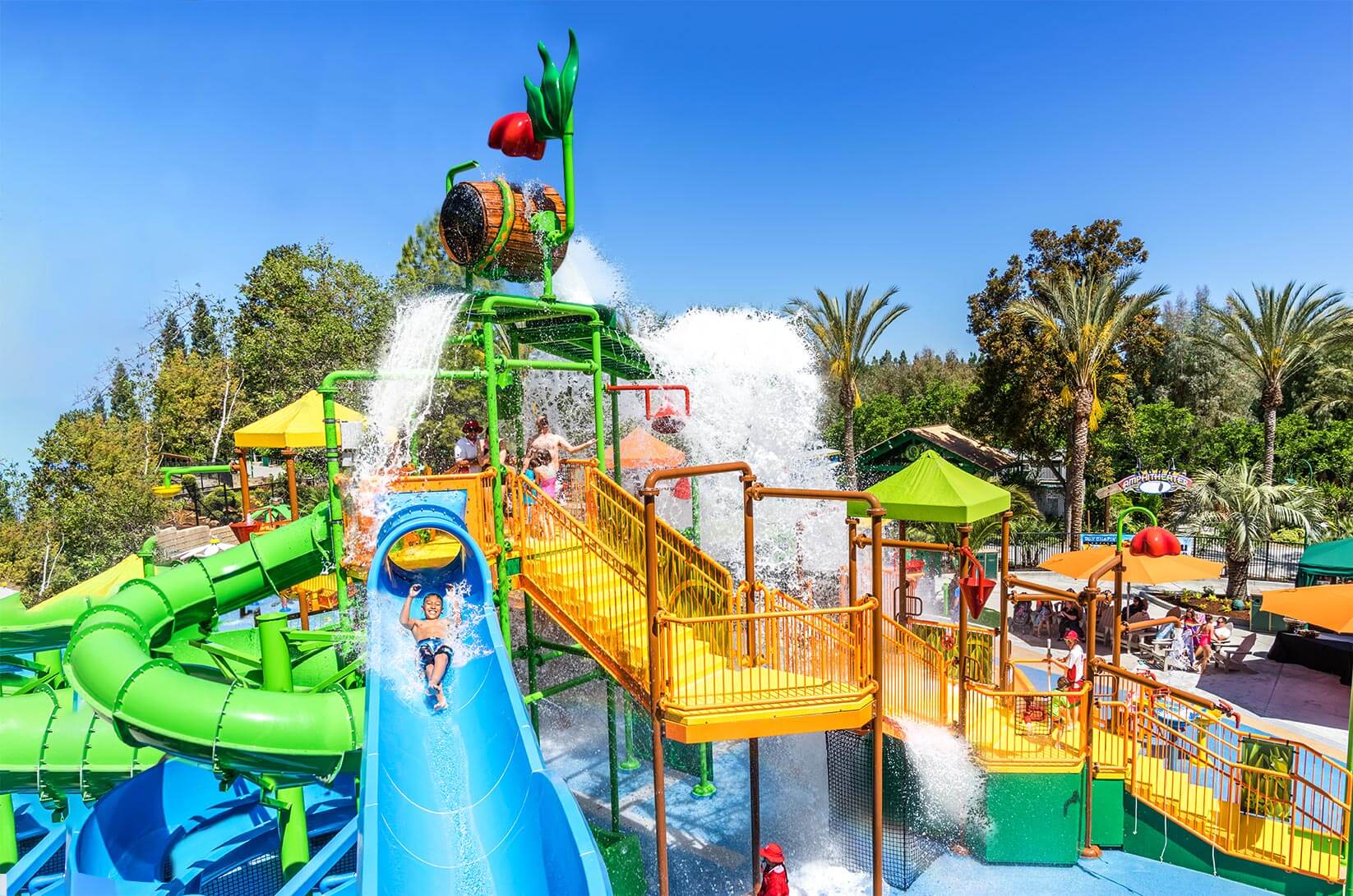 Young boy in blue swim trunks smiling while going down a blue water slide.