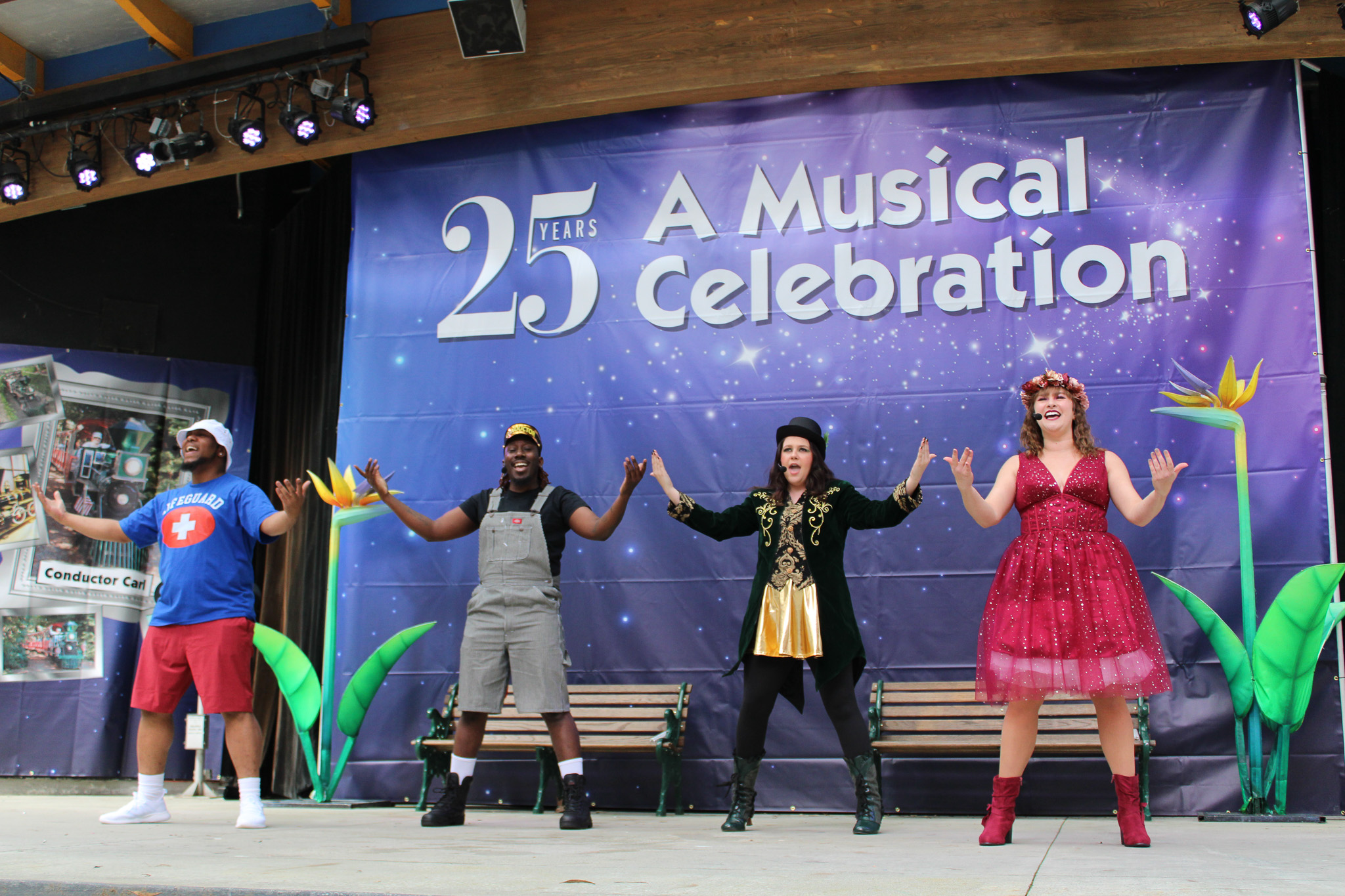 Two women and two men dancing on stage with a purple backdrop behind them while wearing colorful outfits
