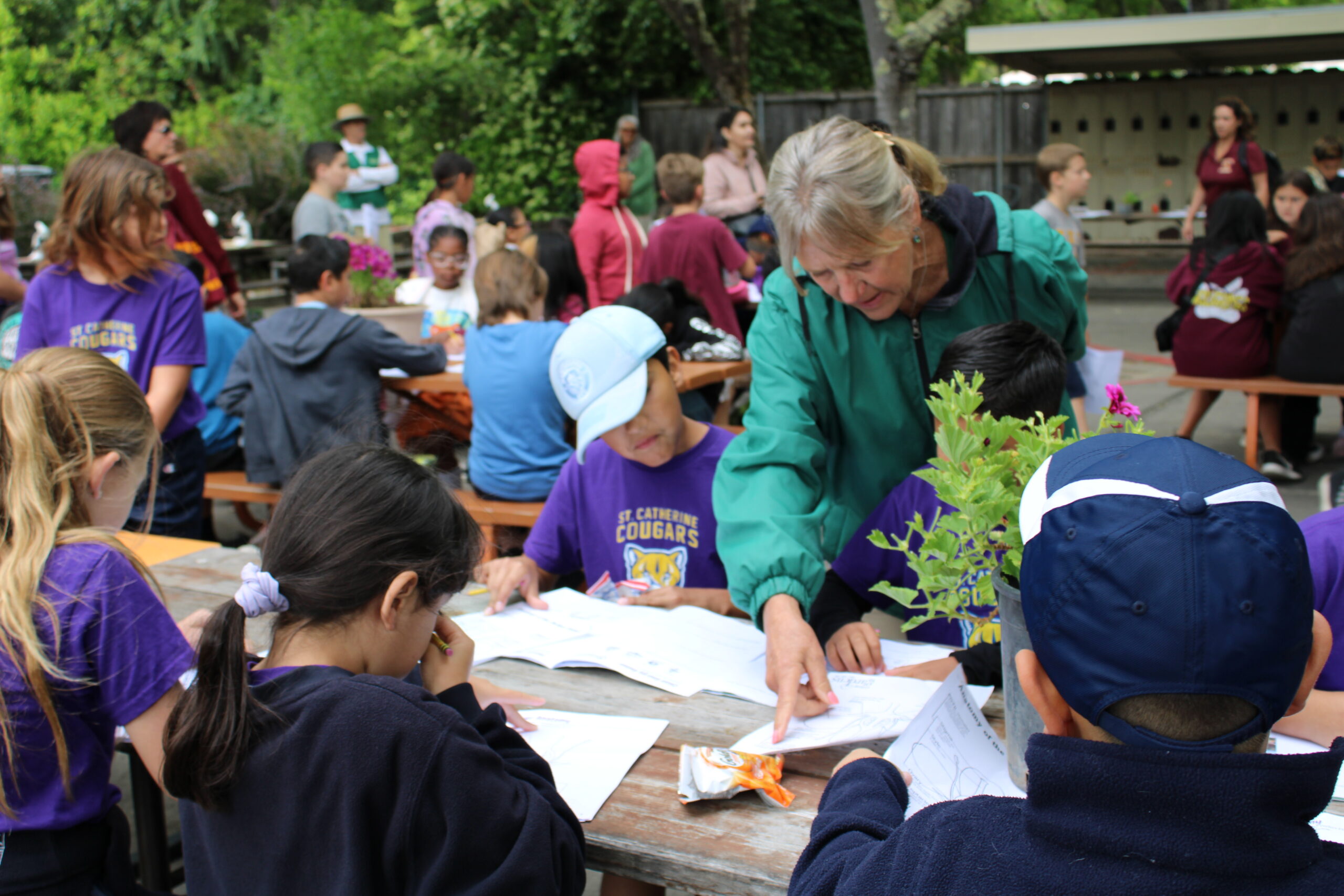 Docent lady assisting children complete their activity sheets on a wooden bench.