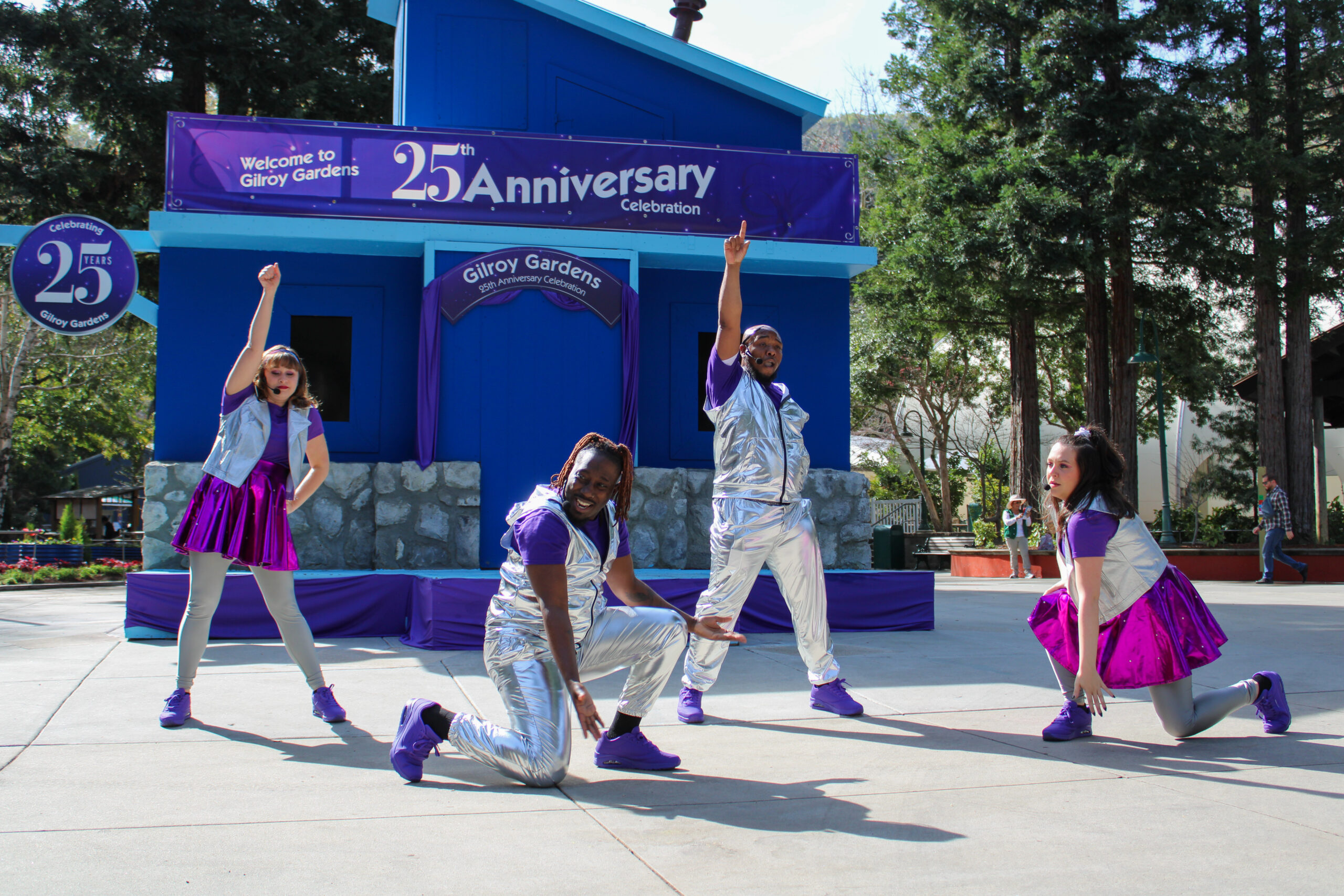 Two women and two men dancing in front of a purple house in silver and purple outfits