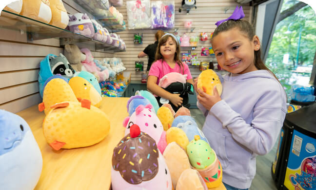 Young girl in purple sweater and bow holding a yellow stuffed animal and girl in pink shirt holding a black and pink stuffed animal
