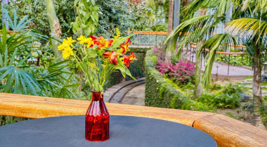 Yellow and red flowers inside of a red vase on-top of a black table