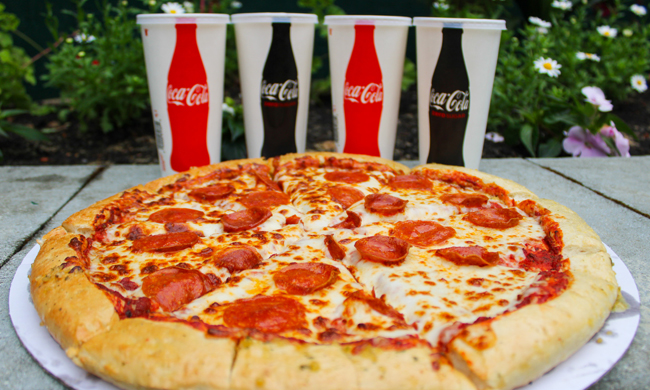 Pepperoni pizza with four cups of soda behind it