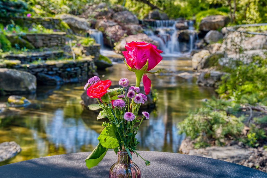 Pink vase filled with pink flowers and roses in front of a waterfall