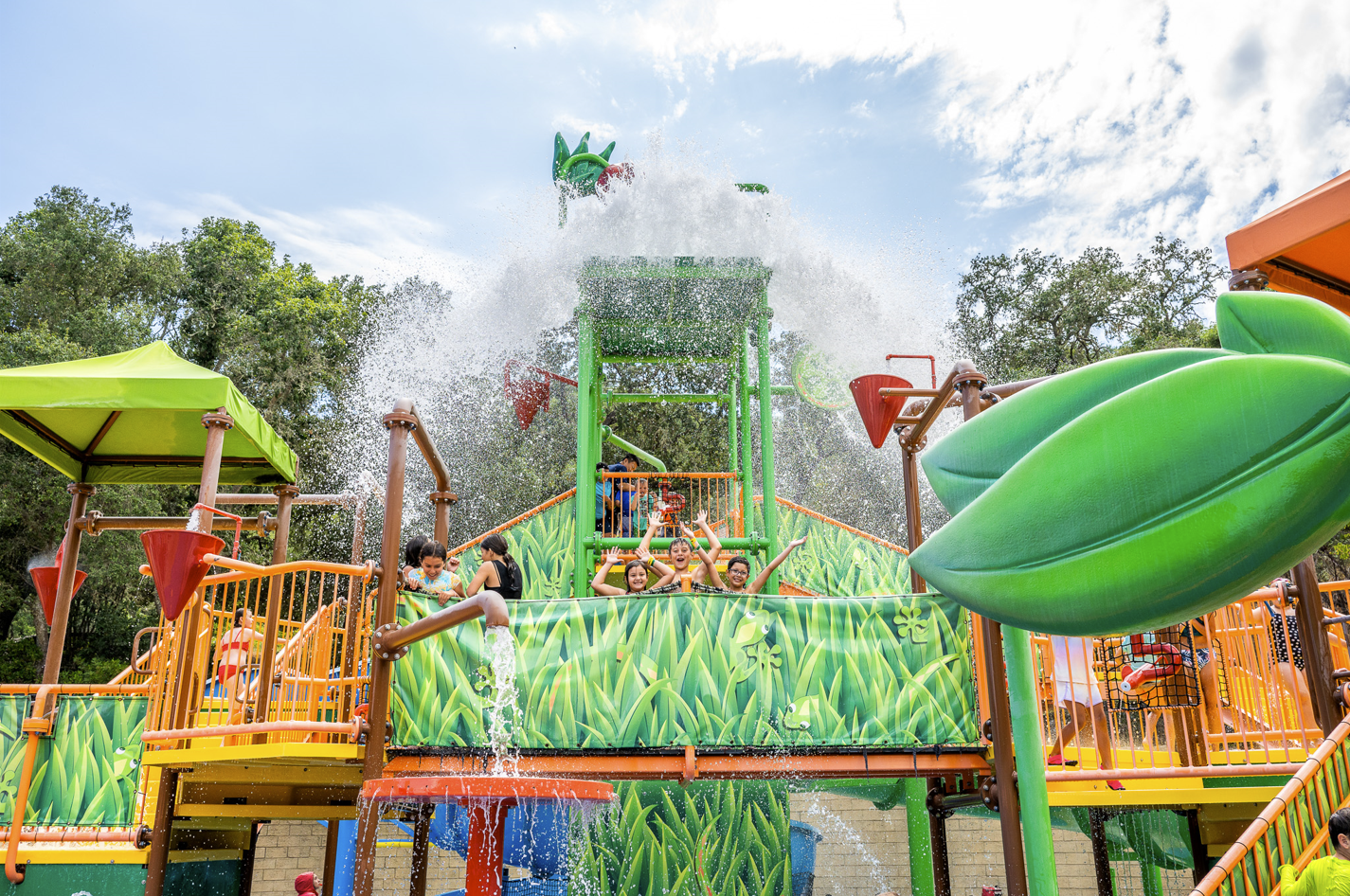 Three children with their hands in the air smiling and laughing while water is spilling from the bucket at Water Oasis