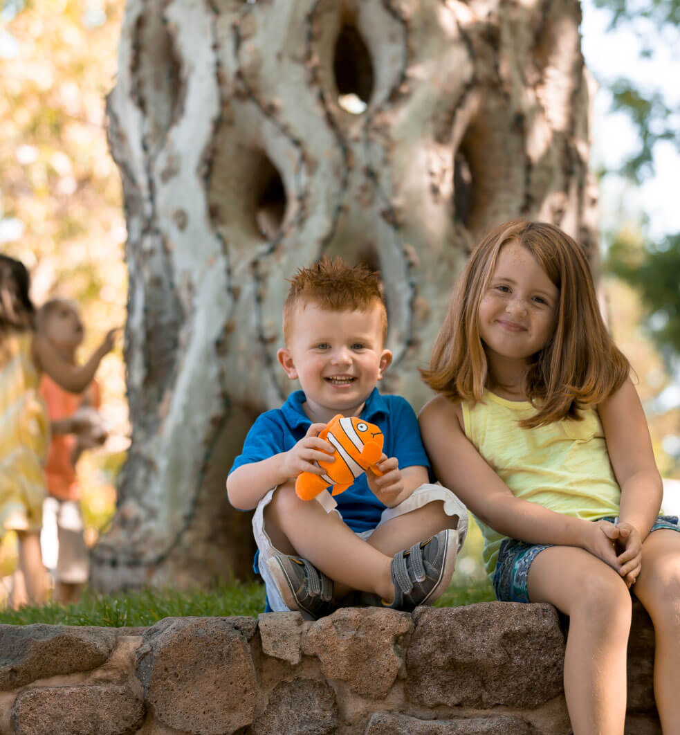 Two children smiling while sitting in front of a basket circus tree