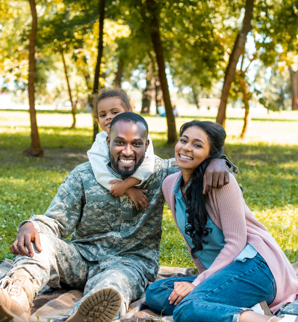 Veteran family smiling while sitting on a light brown blanket