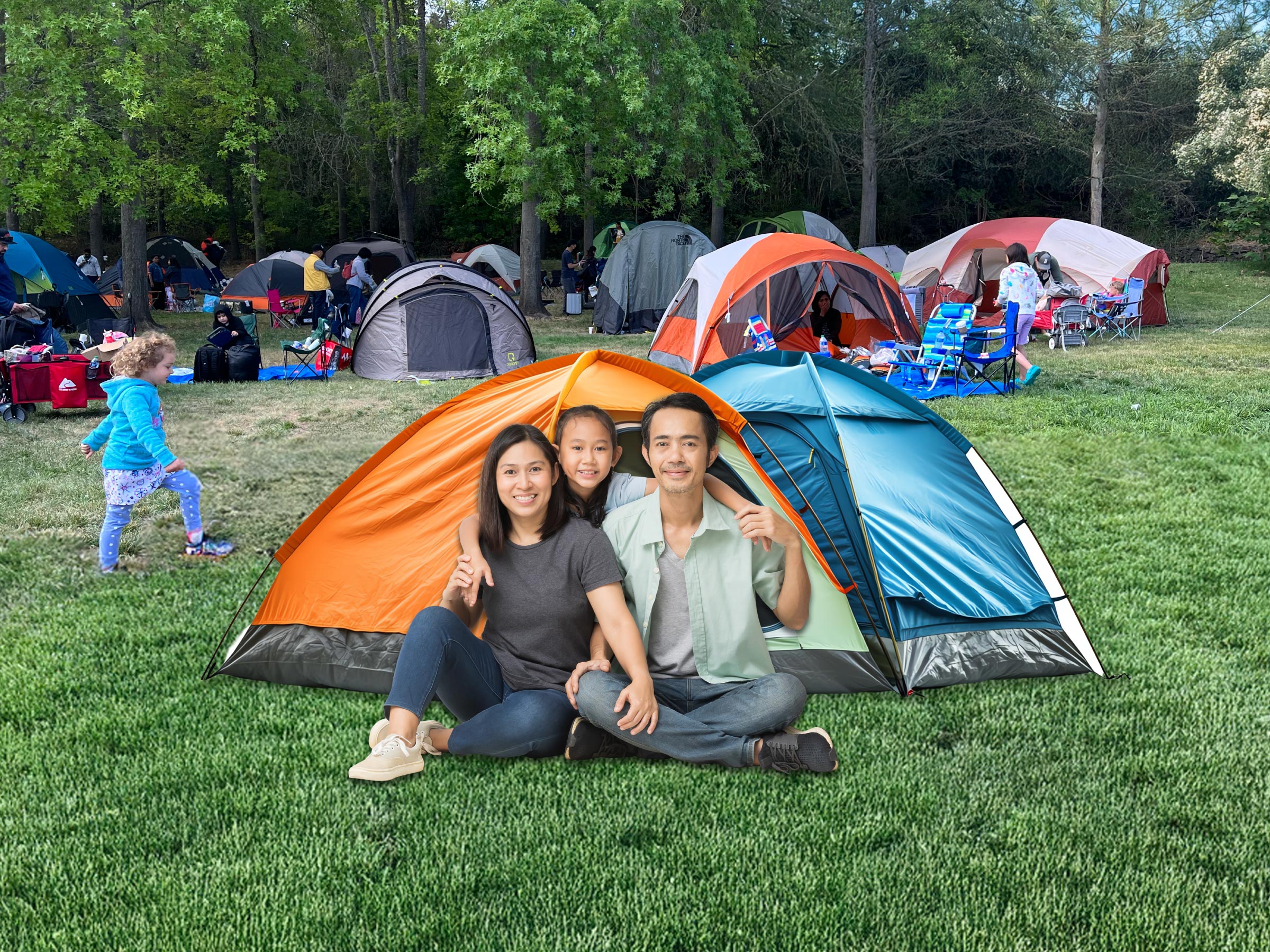 Family of three sitting on the green grass in-front of their orange and blue tent