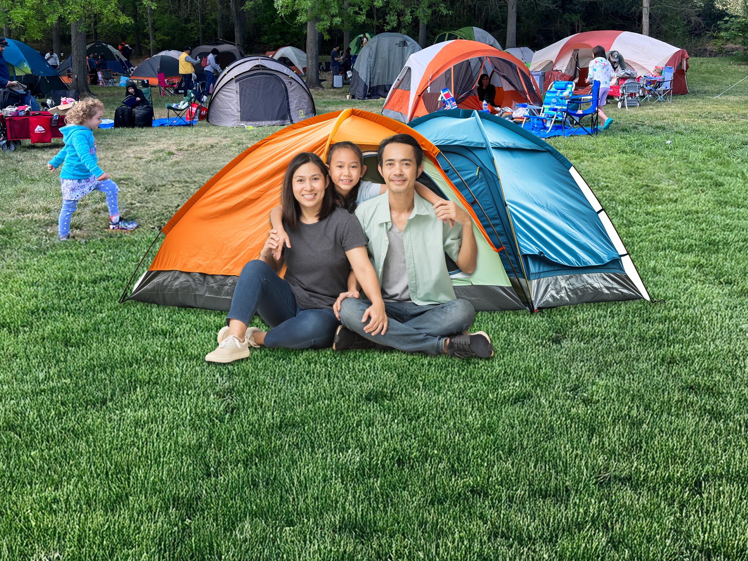 Family of three sitting on the green grass in-front of their orange and blue tent