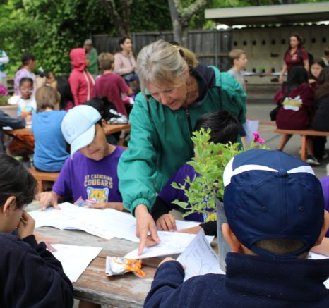 Children completing worksheets while a woman in a green jacket gives them instructions