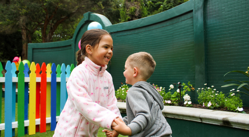 Two young friends holding hands while smiling near white flowers