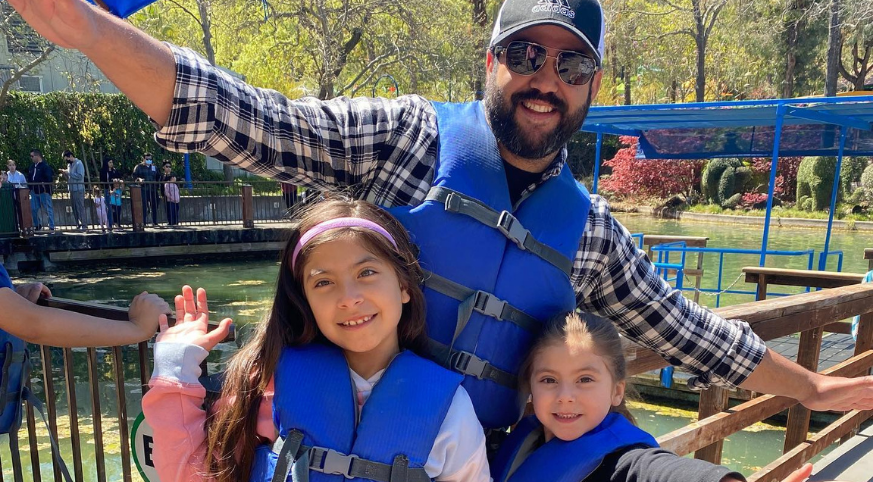 Father with his two young daughters smiling while wearing blue life jackets