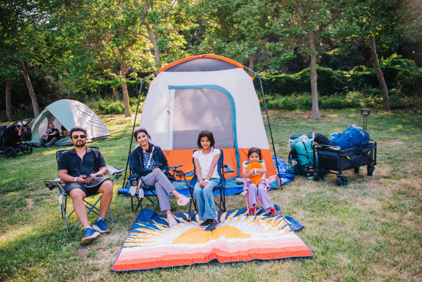 Family sitting on lawn chairs in front of their tan and orange tent