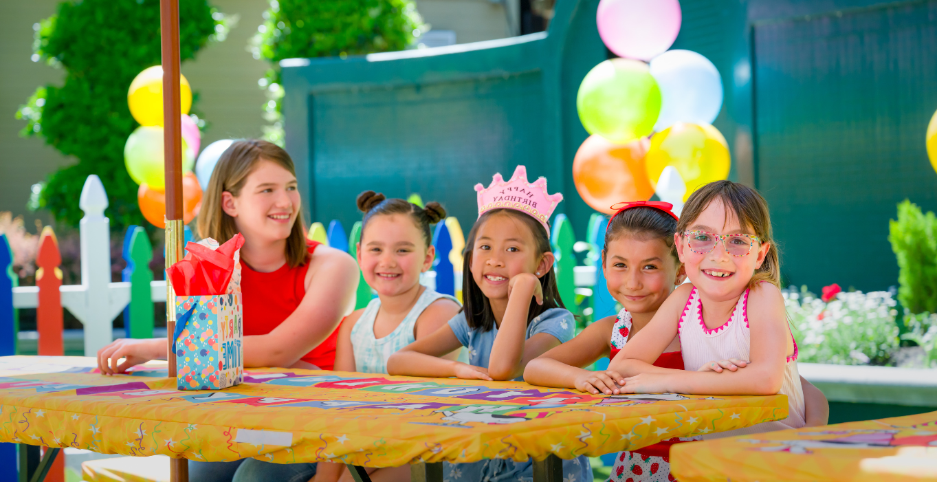 Five young girls smiling at a birthday party with balloon behind them