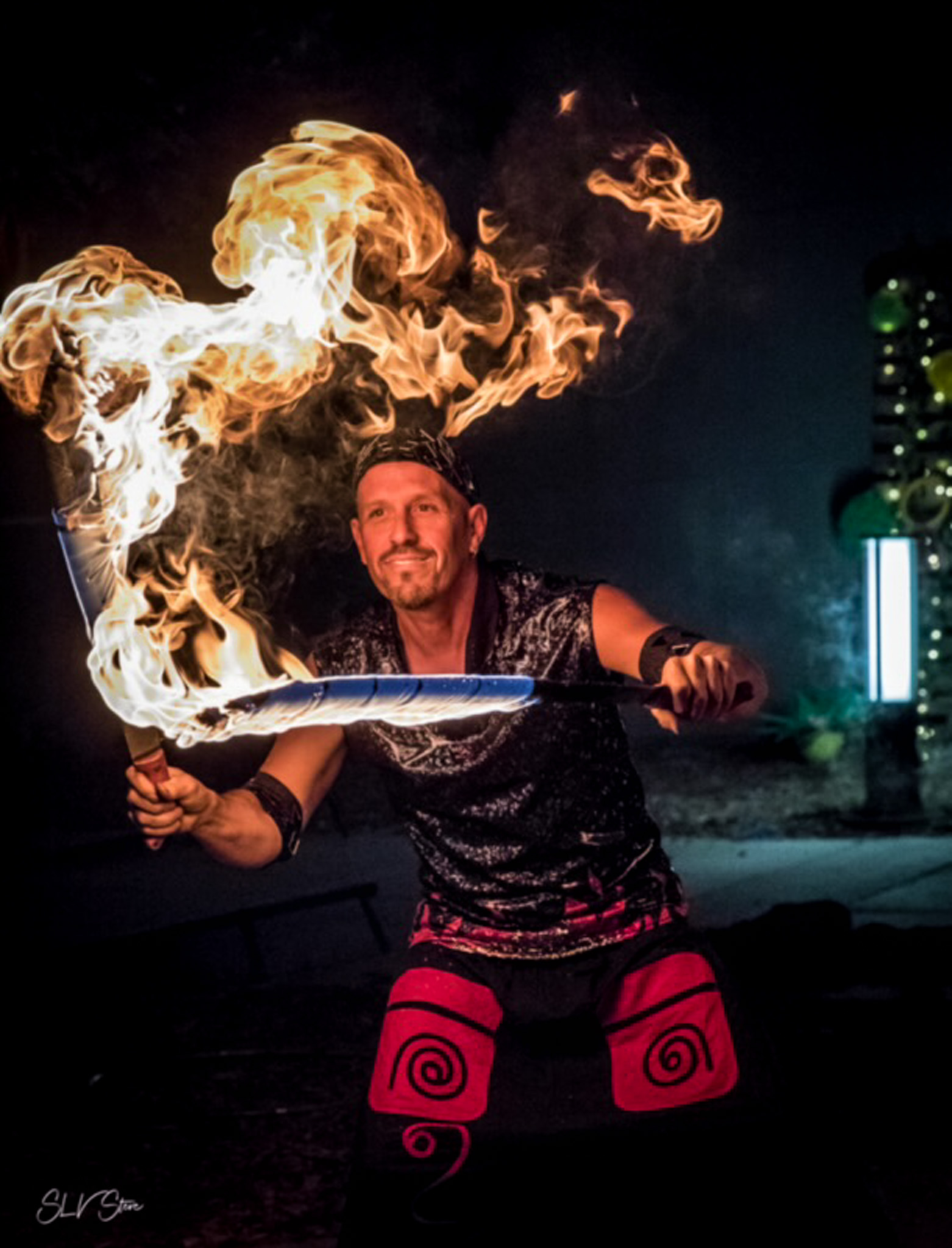 Man smiling holding while doing a fire performance with swords