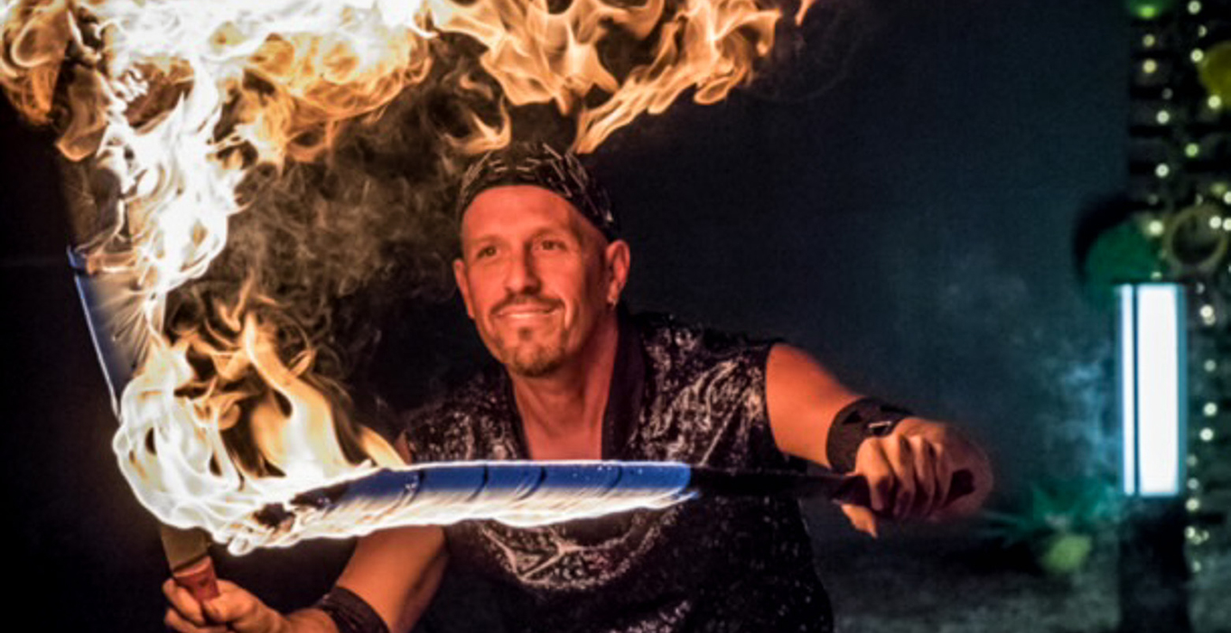 Man smiling holding while doing a fire performance with swords